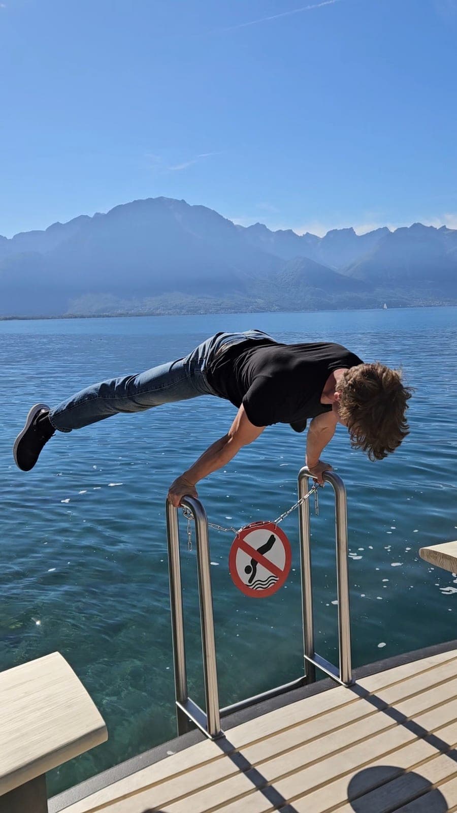 Walking green flag in Prague holding a planche on a lakeside railing with mountains behind him